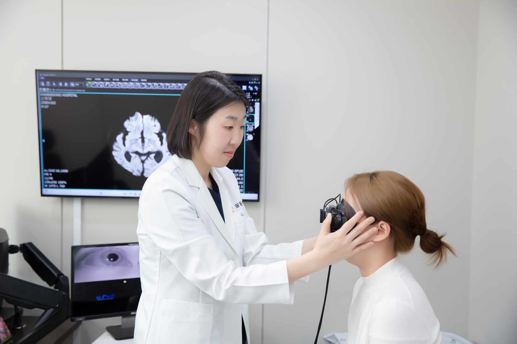 Neurologist recording eye movements, with a brain scan on the monitor
